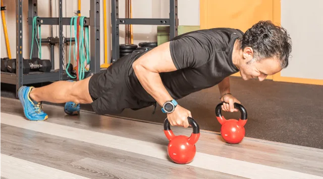A person in a plank position with kettlebells, wearing a Dexcom continuous glucose monitor
