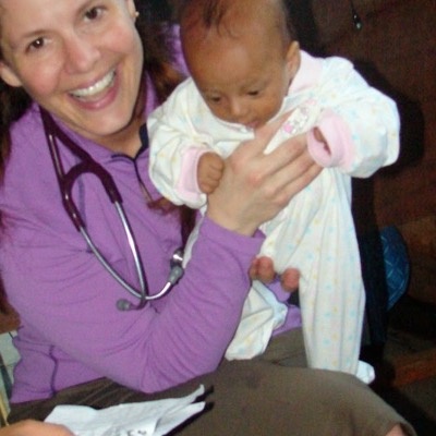 A smiling clinician holding an infant during a medical mission